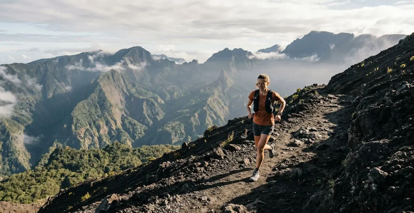 Traileur en pleine ascension sur les sentiers volcaniques de La Réunion avec vue panoramique sur les cirques montagneux