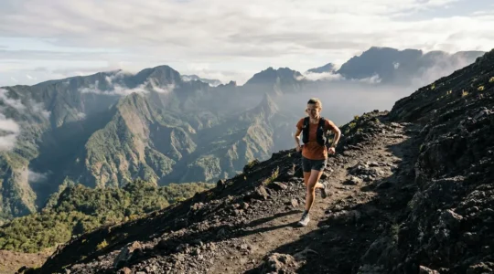 Traileur en pleine ascension sur les sentiers volcaniques de La Réunion avec vue panoramique sur les cirques montagneux