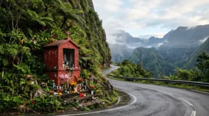 Oratoire rouge de Saint Expédit dans un virage de montagne tropicale à La Réunion avec offrandes et végétation luxuriante