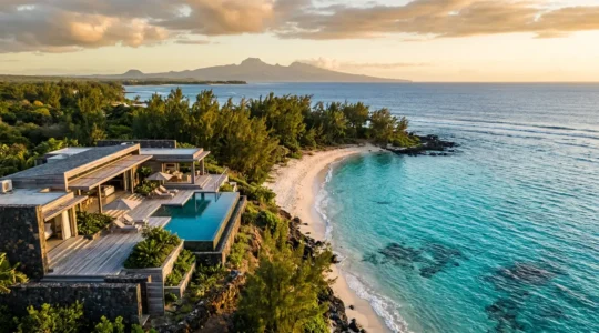 Villa contemporaine avec piscine surplombant un lagon turquoise et une plage de sable blanc bordée de filaos à La Réunion, vue au coucher de soleil