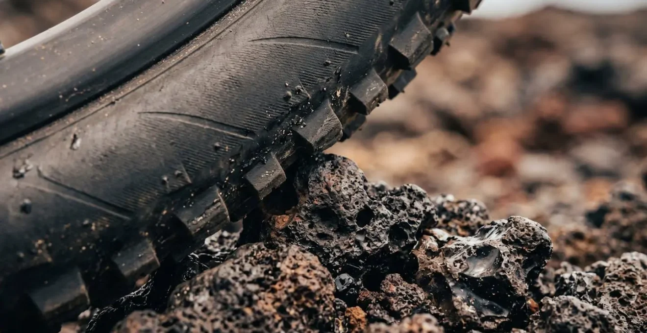 Gros plan sur un pneu VTT en contact avec de la roche volcanique montrant la déformation de la gomme