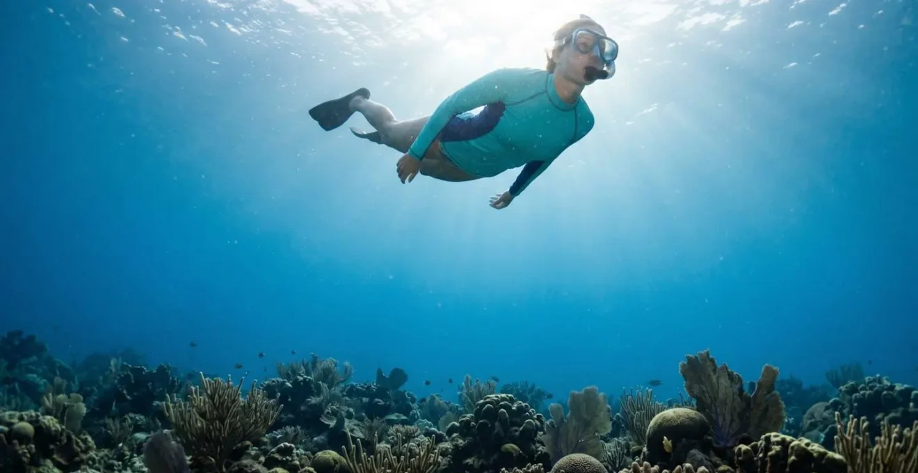 Plongeur portant un lycra anti-UV coloré nageant au-dessus de coraux préservés