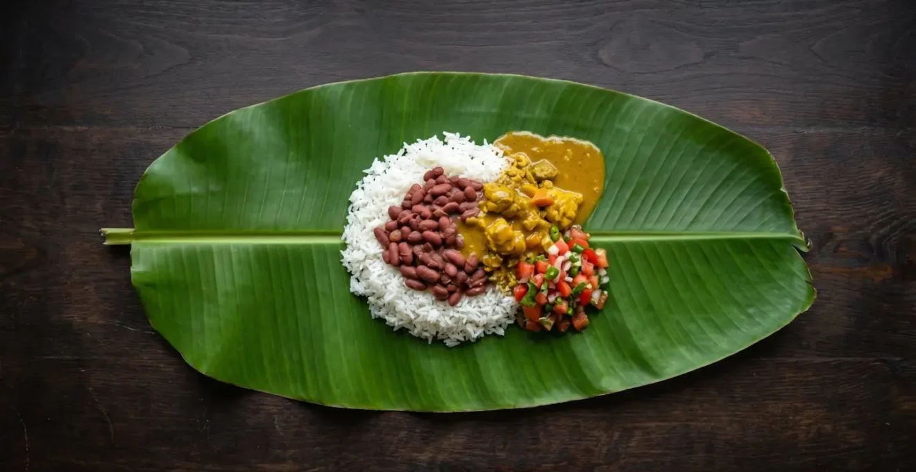 Vue aérienne d'une assiette créole montrant la disposition traditionnelle des aliments : le riz en base, les grains dessus, le cari sur le côté et le rougail en touche finale.