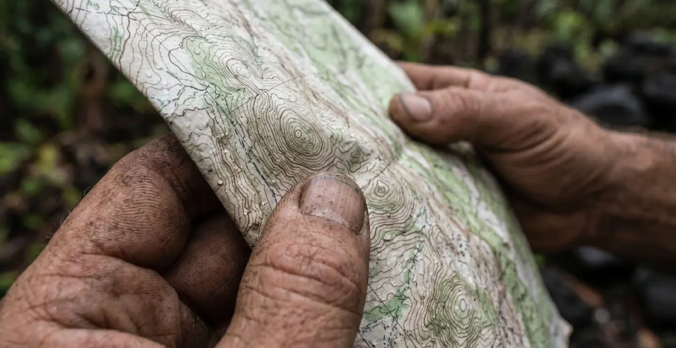 Gros plan sur les mains d'un randonneur tenant une carte topographique pliée dans une ravine tropicale encaissée